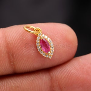 May include: A gold pendant featuring a red gemstone surrounded by smaller white gemstones.
