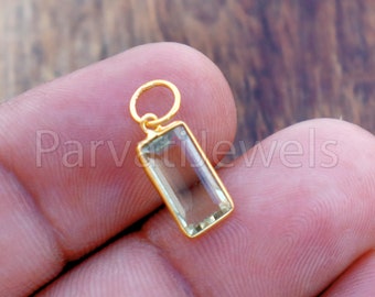 Puede incluir: Un colgante de oro con una piedra rectangular transparente. El colgante está en un dedo.