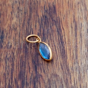 May include: A gold pendant with a blue gemstone in a marquise shape.