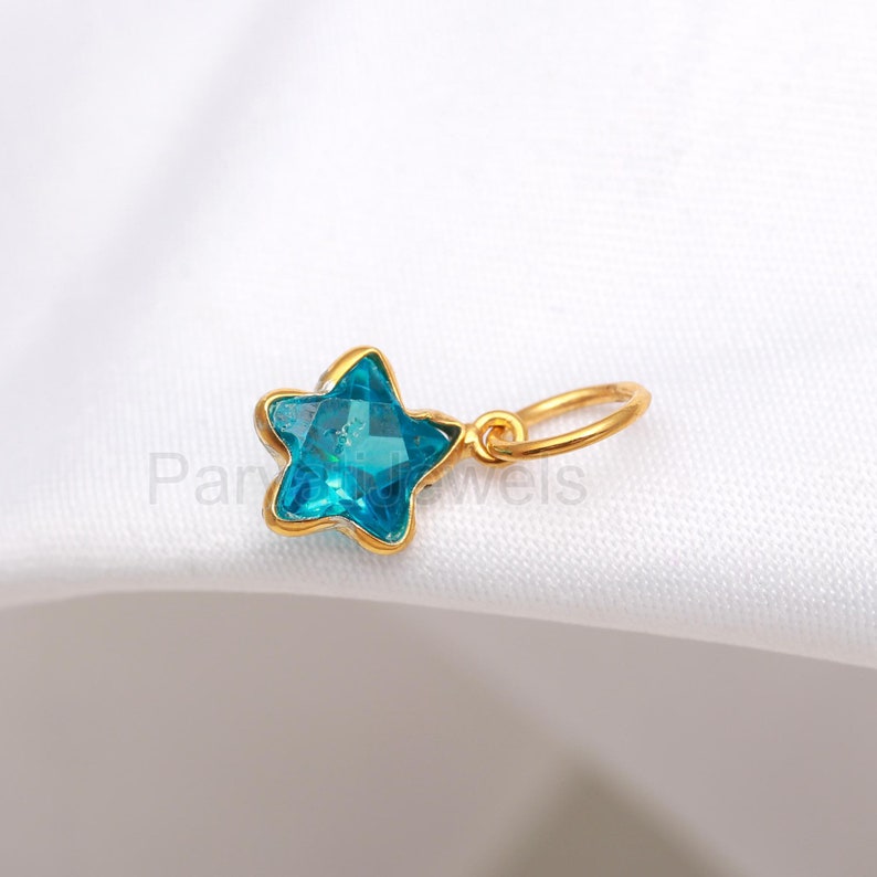May include: A gold star charm with a blue crystal in the center. The charm has a loop for attaching to a necklace or bracelet.