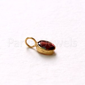 May include: A gold pendant with a red oval gemstone. The pendant has a loop at the top for attaching to a chain.