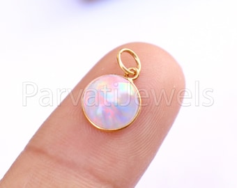 May include: A gold pendant with a round opal gemstone. The opal is iridescent with pink, blue, and white colors.