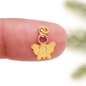 May include: Gold butterfly charm with a red gemstone and the letter "R" engraved on the wings.