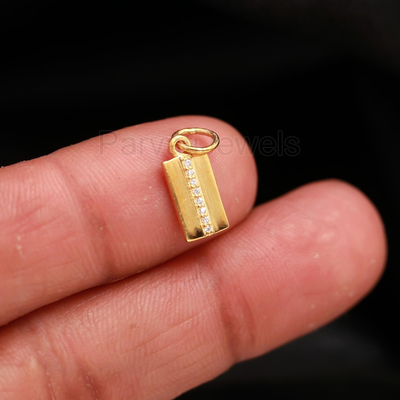 Puede incluir: Un colgante de oro con forma rectangular y una fila de piedras de circonita c&uacute;bica transparentes en el centro.