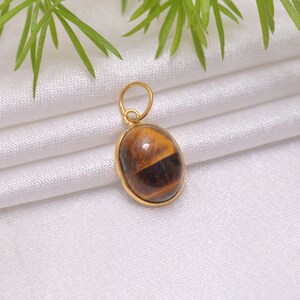 May include: Gold pendant featuring a brown tiger's eye gemstone. The oval-shaped stone has a golden sheen.