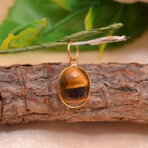 May include: Gold pendant featuring a brown and gold tiger's eye gemstone.