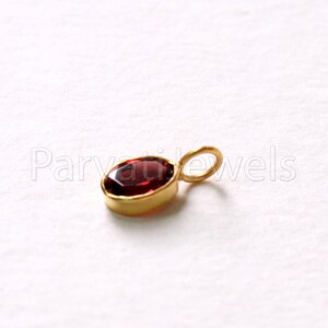 May include: A small gold pendant with a red oval gemstone. The pendant has a loop for attaching to a chain.