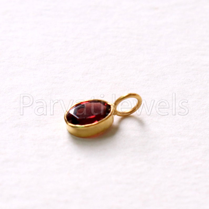 May include: A small gold pendant with a red oval gemstone. The pendant has a loop for attaching to a chain.