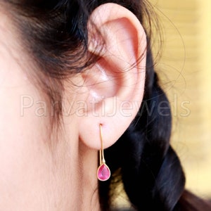 May include: A pair of gold dangle earrings with a teardrop-shaped pink gemstone.
