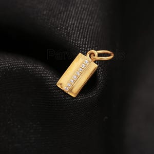 Puede incluir: Un colgante de oro con forma rectangular y una fila de peque&ntilde;as piedras transparentes.