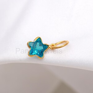 May include: A gold star charm with a blue crystal in the center. The charm has a loop for attaching to a necklace or bracelet.