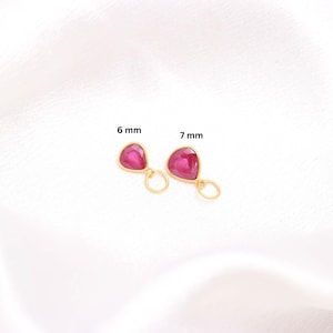 Op de afbeelding: Twee druppelvormige roze edelsteenbedels gezet in goudkleurig metaal, elk voorzien van een kleine ronde ring aan de onderkant. De linkerbedel is gelabeld met 6 mm en de rechterbedel met 7 mm, wat de respectievelijke afmetingen in millimeters aangeeft.