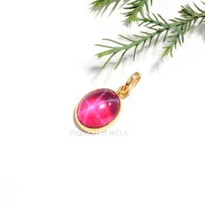 Op de afbeelding: Een gouden hanger met een ovale, dieproze ster-edelsteen met een zichtbaar zesstralig stereffect. De metalen zetting is van glad en gepolijst goud. De tekst PARVATI JEWELS is in het grijs onder de hanger op het witte oppervlak gedrukt.