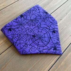 K&ouml;nnte beinhalten: Lilafarbener Bandana mit einem schwarzen Spinnennetz- und Spinnenmuster.