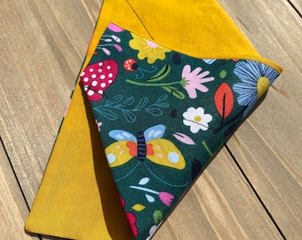 May include: A green fabric bandana with a floral and butterfly print. The bandana is folded in half and has a yellow fabric backing.