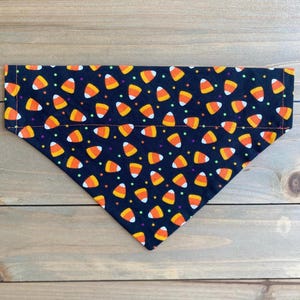 May include: Black bandana with a pattern of orange and yellow candy corn on a black background. The bandana has a white and green polka dot pattern.