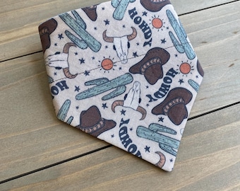 May include: A beige bandana with a repeating pattern of cacti, cowboy hats, and the word "Howdy" in a vintage style font.