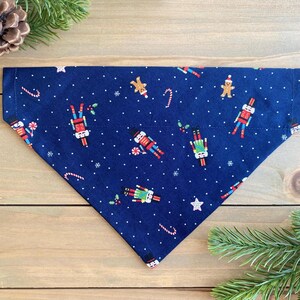 May include: A blue dog bandana with a festive Christmas pattern featuring nutcracker soldiers, candy canes, and snowflakes.