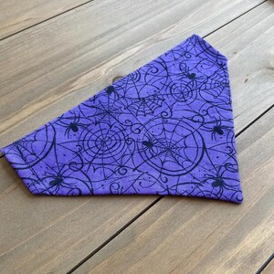 K&ouml;nnte beinhalten: Lilafarbener Bandana mit einem schwarzen Spinnennetz- und Spinnenmuster.