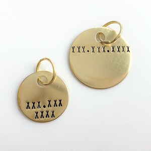 May include: Two gold-colored round metal tags with key rings. The top tag has the text "XXX. XXX. XXXX" engraved on it. The bottom tag has the text "XXX. XXX XXXX" engraved on it.
