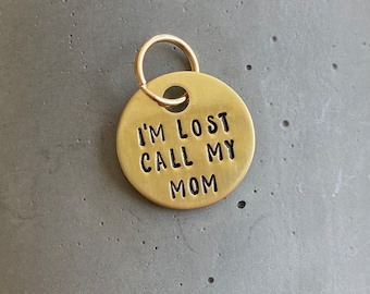 Könnte beinhalten: Ein goldfarbener Hundemarkenanhänger aus Metall mit dem eingravierten Text "I'm lost call my mom".
