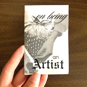 Puede incluir: Una imagen en blanco y negro de una mano sosteniendo una fresa. El texto "on being an Artist" está impreso en la imagen.