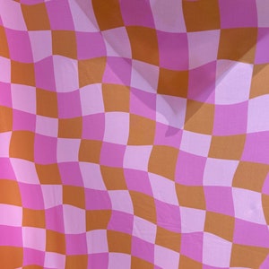 May include: A pink and brown checkered fabric with a wavy pattern. The fabric is made of a soft, lightweight material and has a subtle sheen.