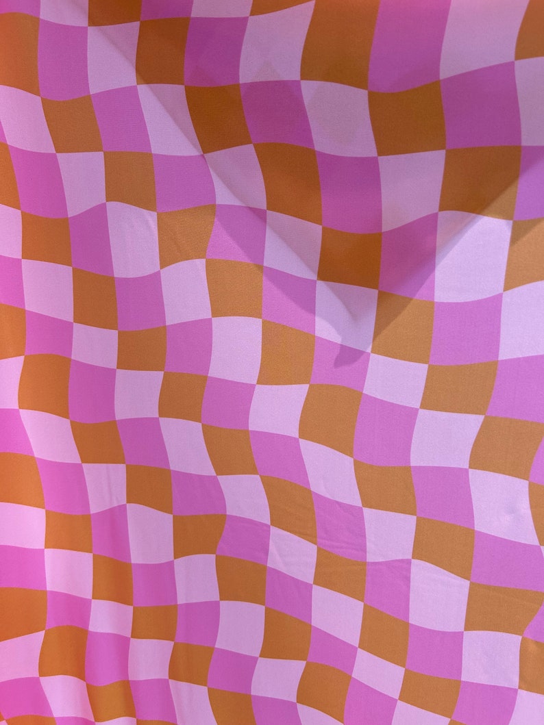 May include: A pink and brown checkered fabric with a wavy pattern. The fabric is made of a soft, lightweight material and has a subtle sheen.