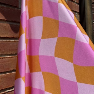 May include: A pink and orange checkered fabric with a wavy pattern. The fabric is folded and draped over a brick wall.