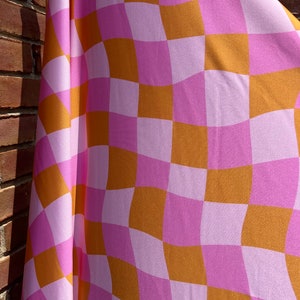 May include: A pink and orange checkered fabric with a wavy pattern. The fabric is draped over a brick wall.
