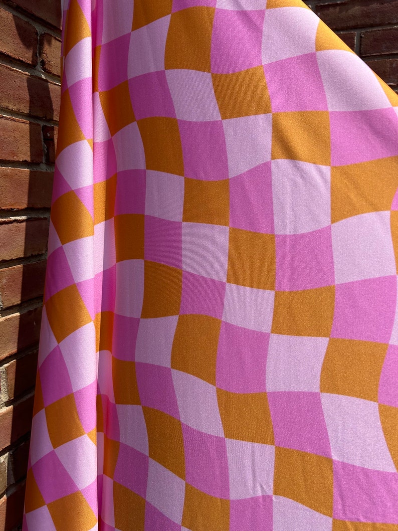 May include: A pink and orange checkered fabric with a wavy pattern. The fabric is draped over a brick wall.