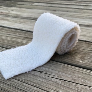 May include: A white, fluffy, rolled up piece of fabric. The fabric has a soft, fuzzy texture.