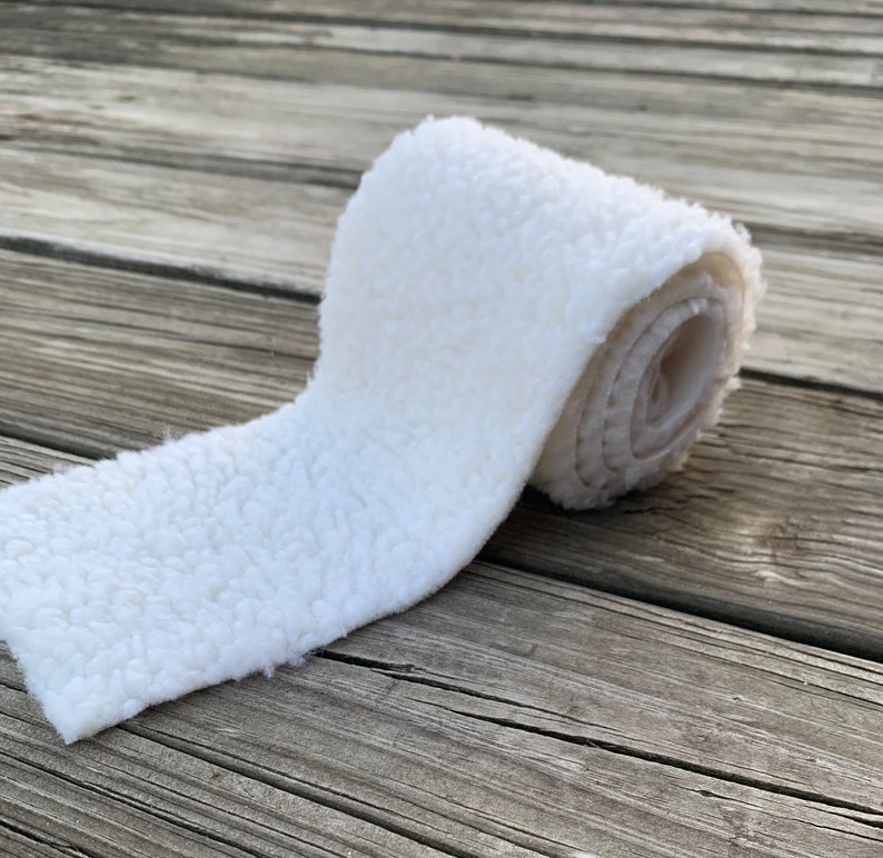 May include: A white, fluffy, rolled up piece of fabric. The fabric has a soft, fuzzy texture.