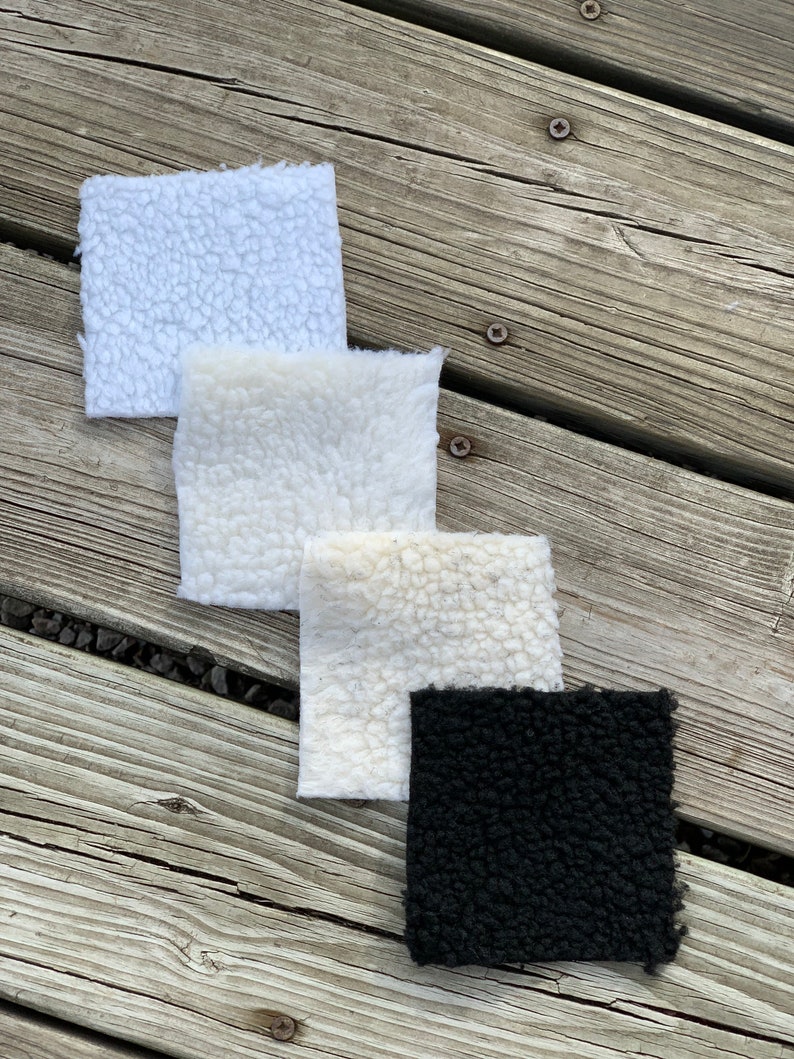 May include: Four fabric swatches, three white and one black, with a fuzzy texture. The swatches are arranged in a vertical stack on a wooden surface.