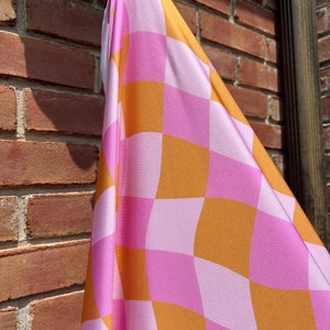 May include: A pink and orange checkered fabric with a wavy pattern. The fabric is hanging from a hook.