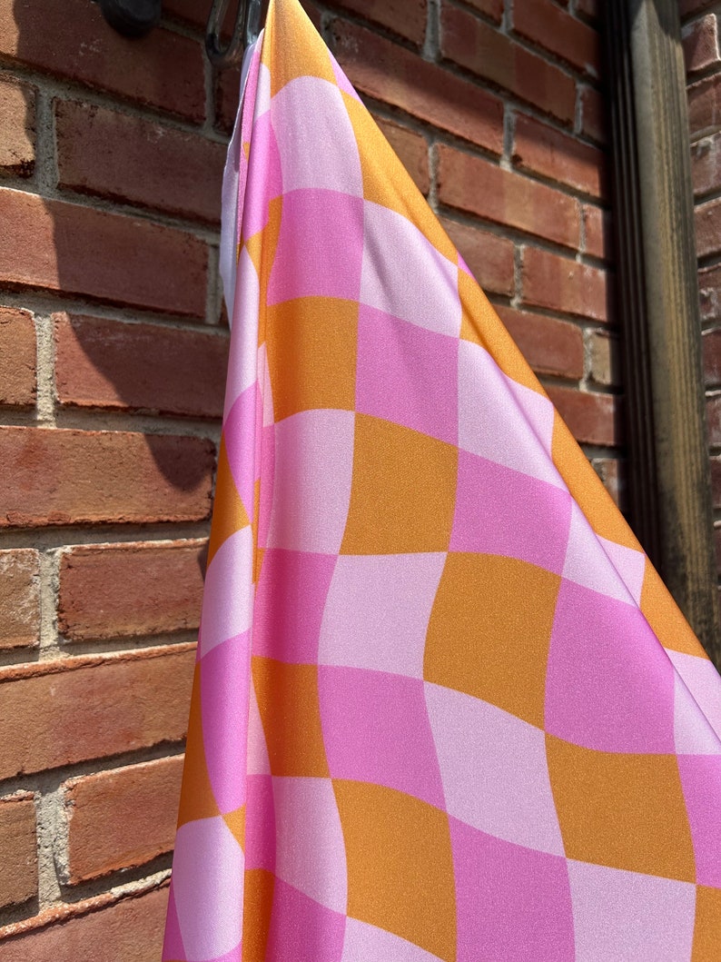 May include: A pink and orange checkered fabric with a wavy pattern. The fabric is hanging from a hook.