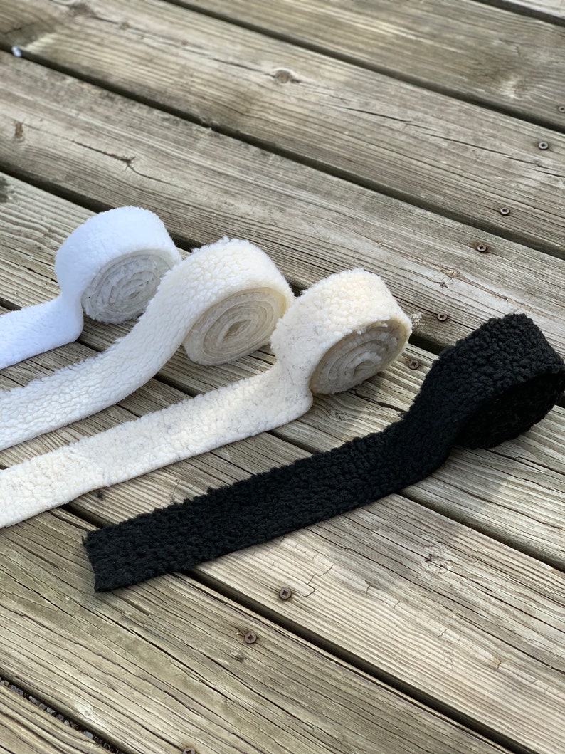 May include: Four rolls of faux fur fabric in white, cream, and black. The fabric is soft and fluffy, and it would be perfect for making clothing, accessories, or home decor.