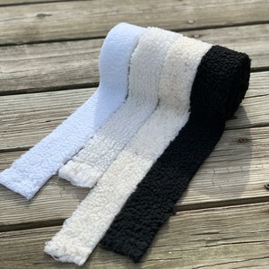 May include: Three rolls of faux fur fabric in white, cream, and black. The fabric is soft and fluffy, and it would be perfect for making blankets, cushions, or other home decor items.