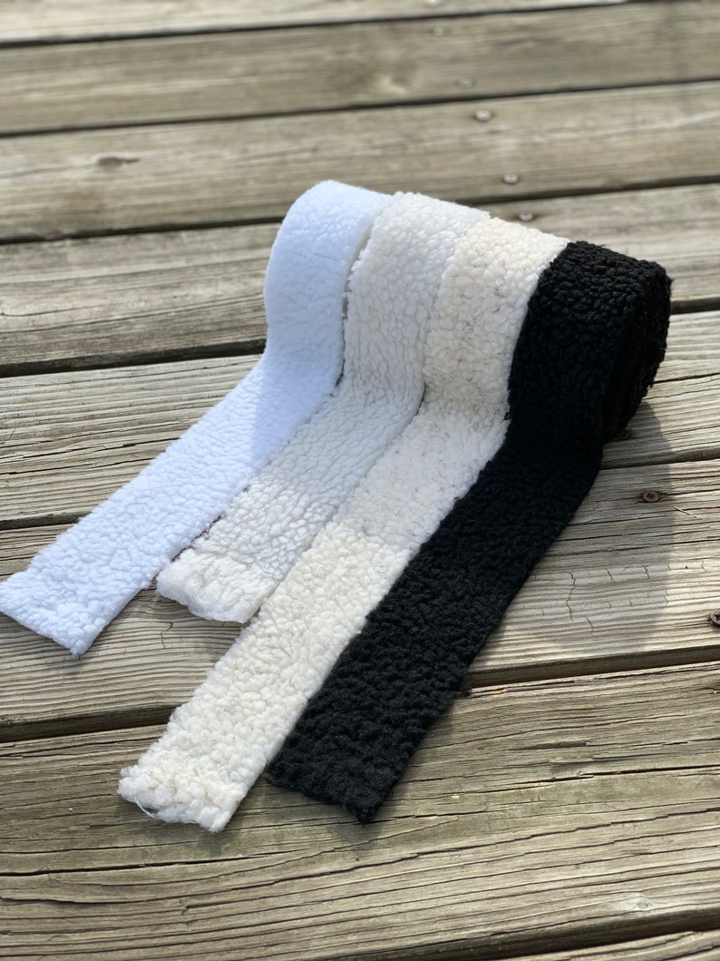 May include: Three rolls of faux fur fabric in white, cream, and black. The fabric is soft and fluffy, and it would be perfect for making blankets, cushions, or other home decor items.