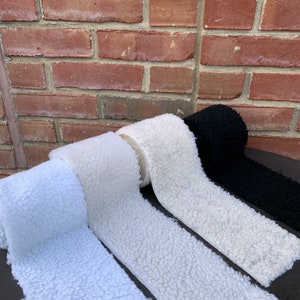 May include: Four rolls of white faux fur fabric, with one roll of black faux fur fabric in the background.