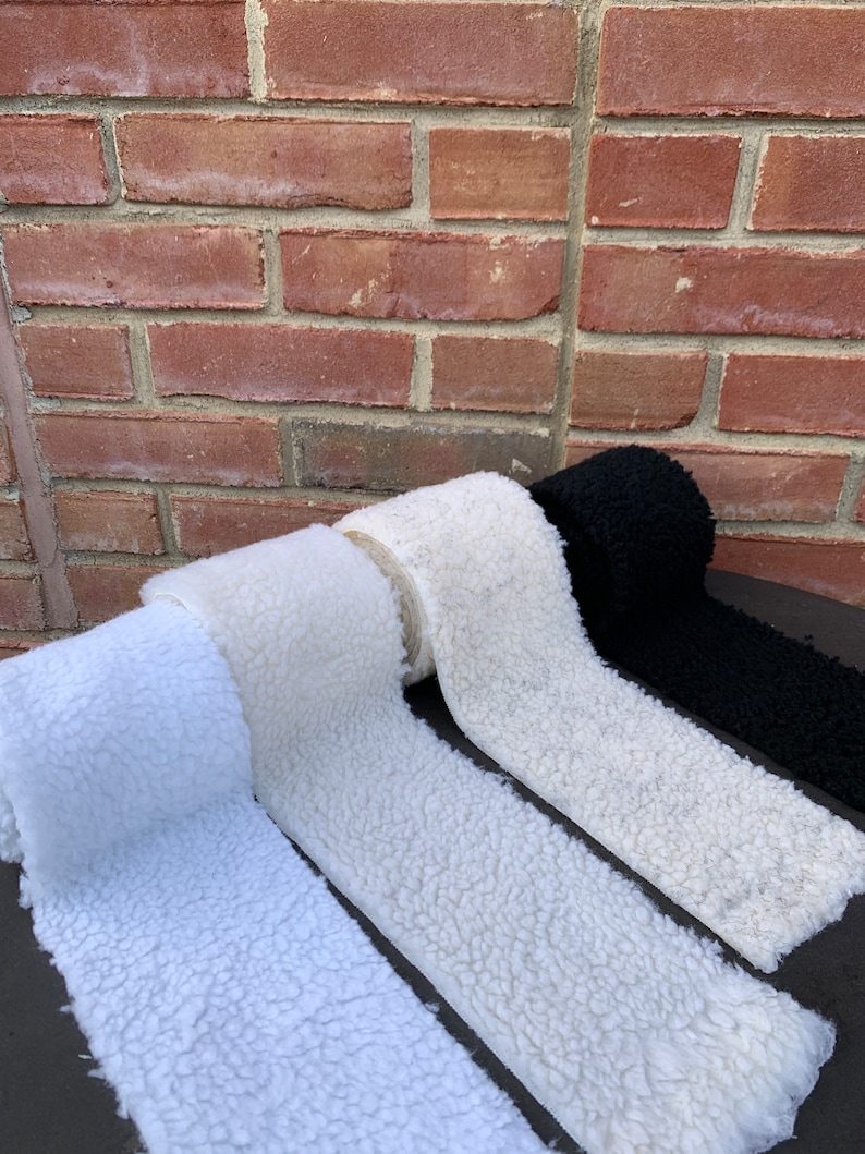 May include: Four rolls of white faux fur fabric, with one roll of black faux fur fabric in the background.