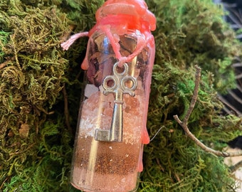 May include: A small glass bottle filled with pink Himalayan salt, dried herbs, and a silver key. The bottle is sealed with pink wax.
