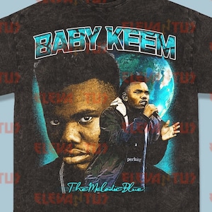 May include: Black t-shirt with a vintage-style graphic of rapper Baby Keem performing in front of a blue and green globe. The text "BABY KEEM" is printed in large, bold letters at the top of the graphic. The text "The Melodic Blue" is printed in a smaller font below the graphic.