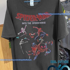 Pode incluir: Camiseta preta com uma estampa gr&aacute;fica dos personagens do Homem-Aranha do filme "Spider-Man: Into the Spider-Verse". O texto "Spider-Man: Into the Spider-Verse" est&aacute; impresso em letras vermelhas e brancas na camiseta.