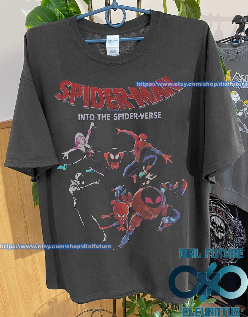 Pode incluir: Camiseta preta com uma estampa gr&aacute;fica dos personagens do Homem-Aranha do filme "Spider-Man: Into the Spider-Verse". O texto "Spider-Man: Into the Spider-Verse" est&aacute; impresso em letras vermelhas e brancas na camiseta.