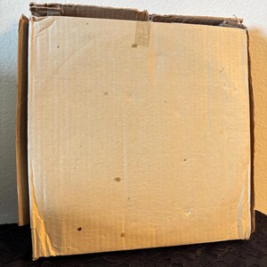 Peut inclure: Une bo&icirc;te en carton rectangulaire partiellement ouverte. La bo&icirc;te est en carton ondul&eacute; et de couleur brun clair. Les bords de la bo&icirc;te sont l&eacute;g&egrave;rement us&eacute;s et il y a du ruban adh&eacute;sif sur le dessus.