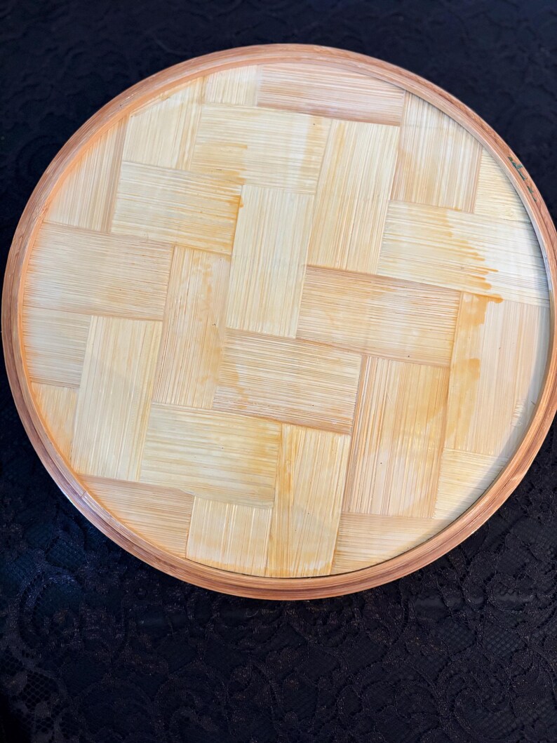 Peut inclure: Plateau rond en bambou tress&eacute;, avec un bord marron clair et une surface tiss&eacute;e naturelle de couleur claire. Le design du plateau pr&eacute;sente un motif de tissage en panier, mettant en valeur le grain naturel du bois.