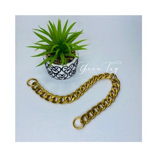 May include: A gold chain with two large, round, open links. The chain is lying on a white surface.