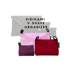 Puede incluir: Organizador Kirigami en forma de V en tonos rosa y burdeos. El organizador tiene un diseño en forma de V y está hecho de fieltro. La imagen también muestra un clutch Kirigami en el fondo. Se muestra el texto "KIRIGAMI V-SHAPE ORGANIZER".