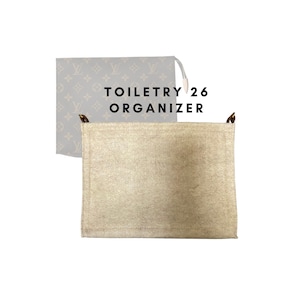 May include: A beige toiletry organiser with brown leather accents and the text "TOILETRY 26 ORGANISER" printed on the front.